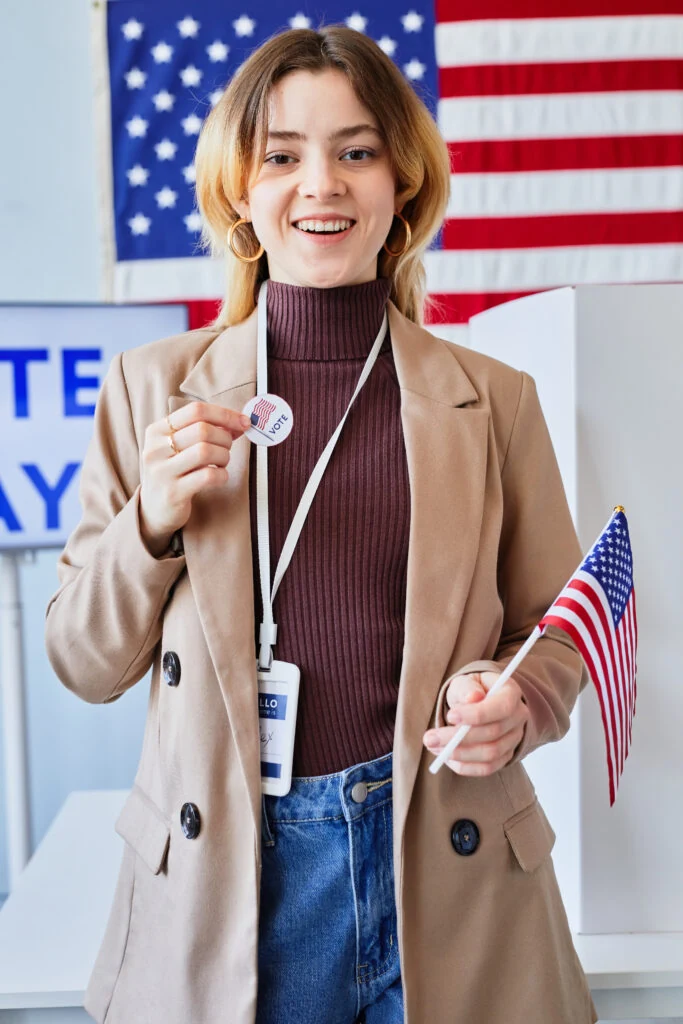 A young woman holding small American flags and wearing a voter sticker at a polling place